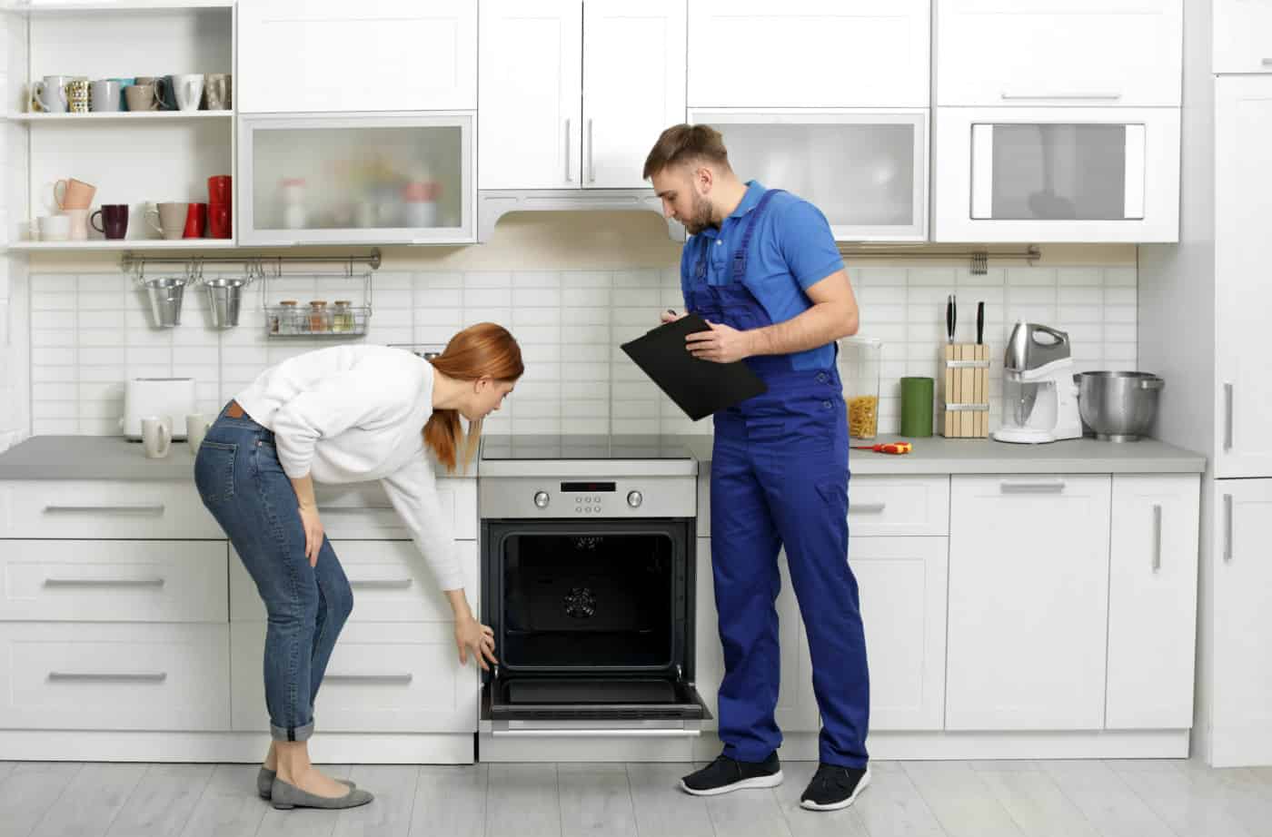 A woman and home repair technician inspecting oven together during scheduled kitchen appliance repair appointment.