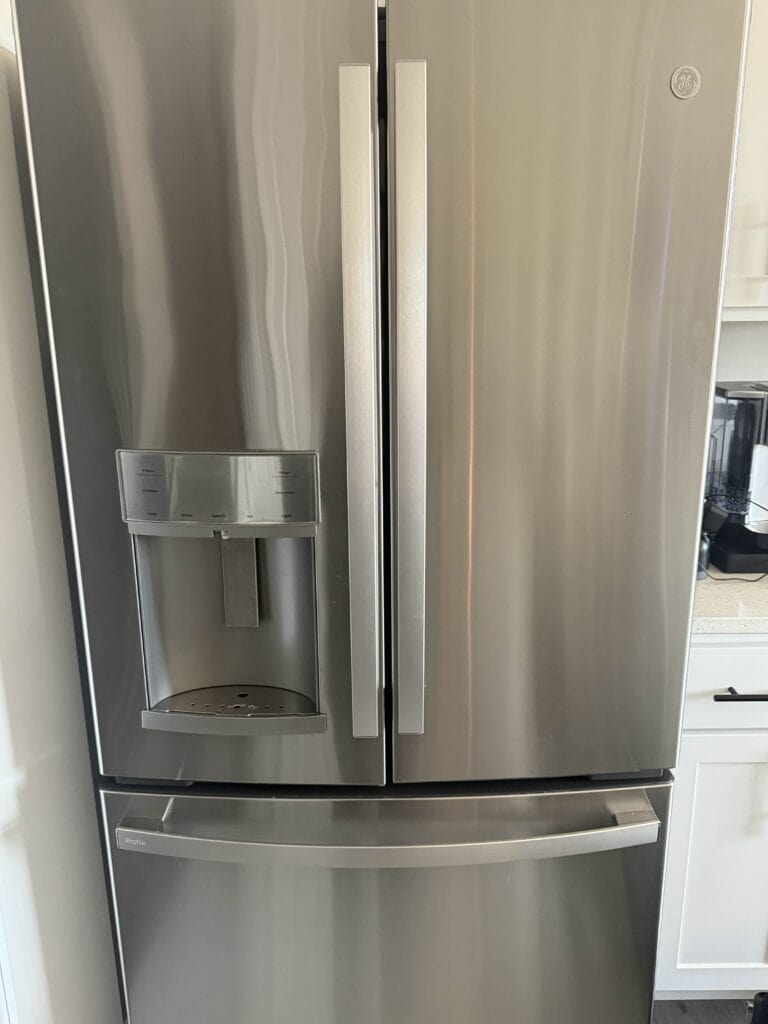 Stainless steel refrigerator with built-in ice maker showing water dispenser and freezer drawer in modern kitchen.