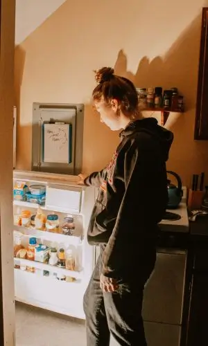 Woman inspecting the inside of her refrigerator at home, checking for issues—reminder to ask: is your fridge running?