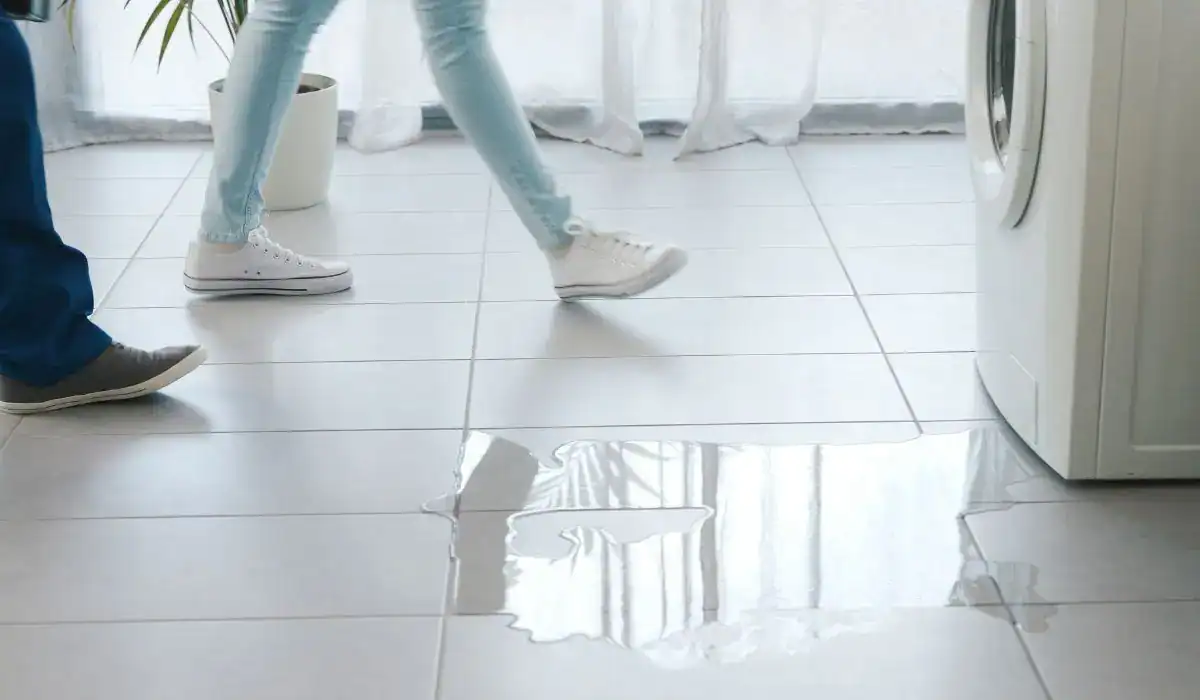 Washing machine leaking water on laundry room tile floor.
