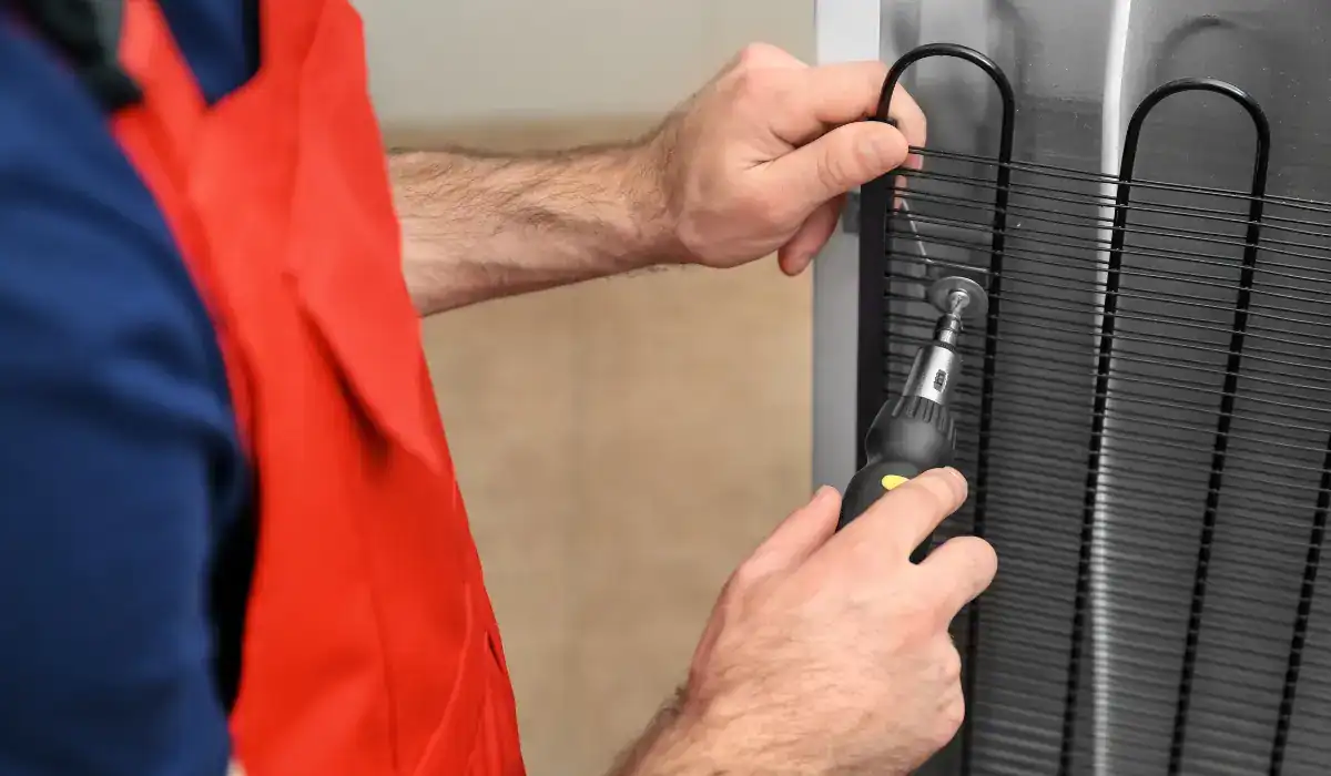 Technician cleaning refrigerator condenser coils during winter appliance maintenance to improve efficiency and prevent breakdowns.